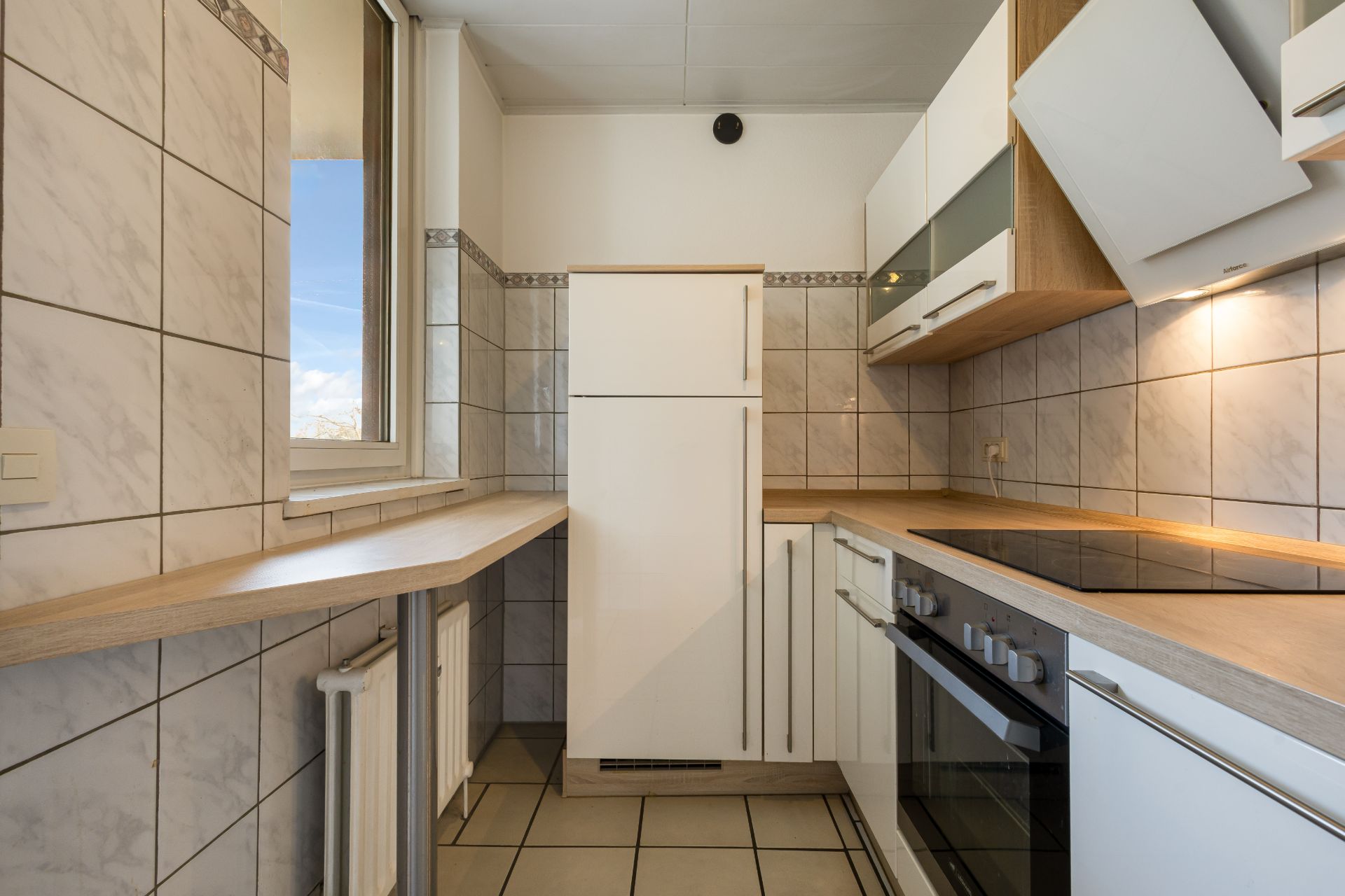 Moderne Einbauküche mit weißem Kühlschrank, Herd, Hängeschränken und Fenster.