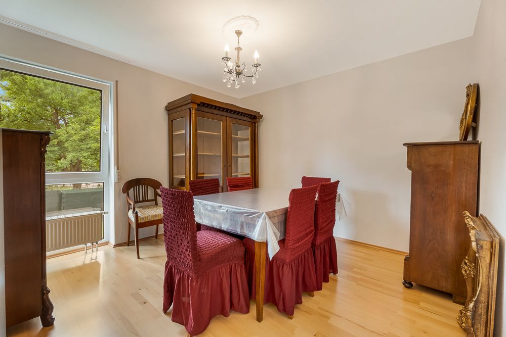 Esszimmer mit Holztisch, sechs rot bezogenen Stühlen und Vitrine, großes Fenster links.