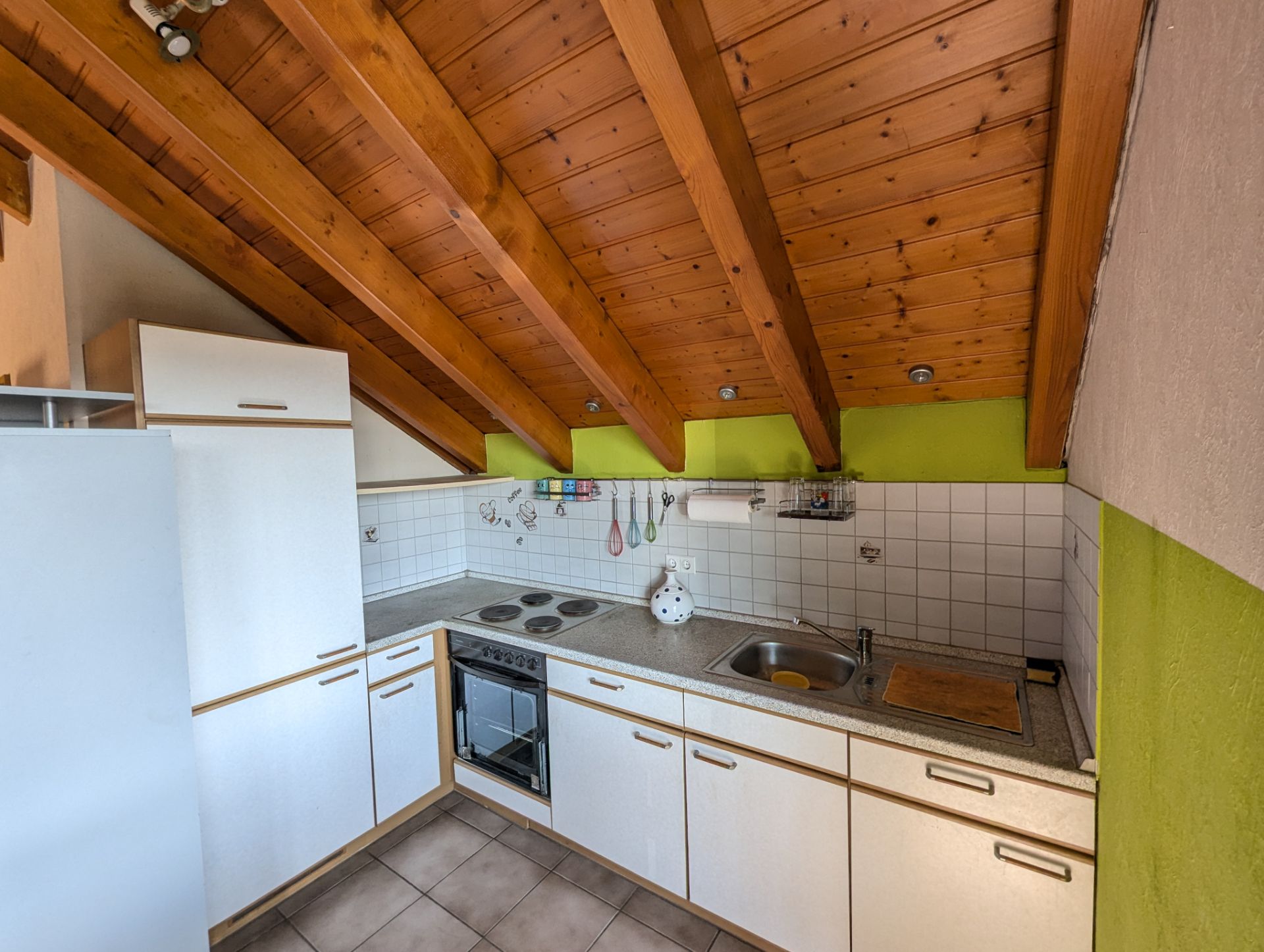 Kleine Einbauküche mit weißer Einrichtung, Holzdecke und grün gestrichenen Wänden.
