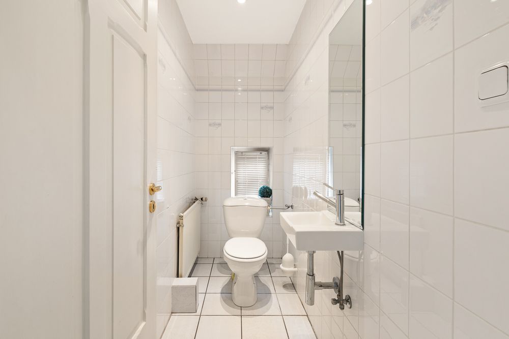 Helles, schmales Badezimmer mit weißer Toilette, kleinem Waschbecken und Fenster.