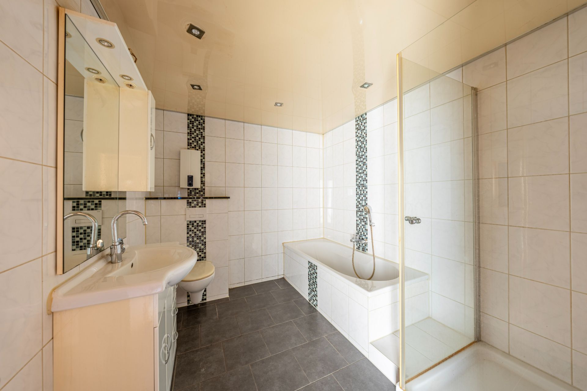 Modernes Badezimmer mit Badewanne, Dusche, Waschbecken und Toilette auf dunklem Fliesenboden.