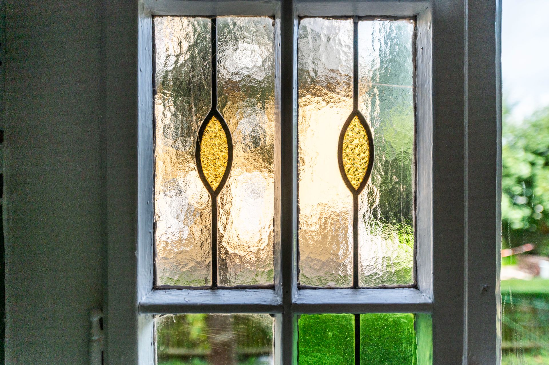 Buntes Bleiglasfenster mit gelben und grünen Elementen in einem Wohnhaus.