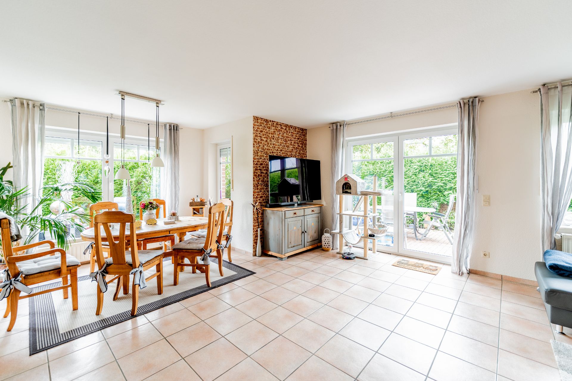 Helles Wohnzimmer mit Essbereich, Fernseher, Holzmöbeln und Zugang zur Terrasse.