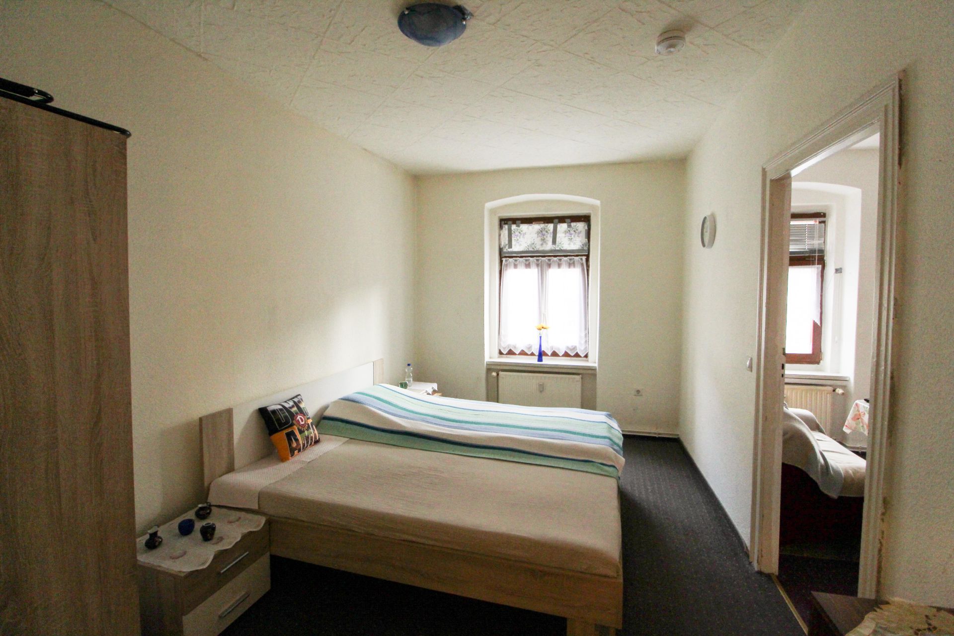 Schlafzimmer mit zwei Einzelbetten, Fenster, Nachttisch und Blick in ein weiteres Zimmer.
