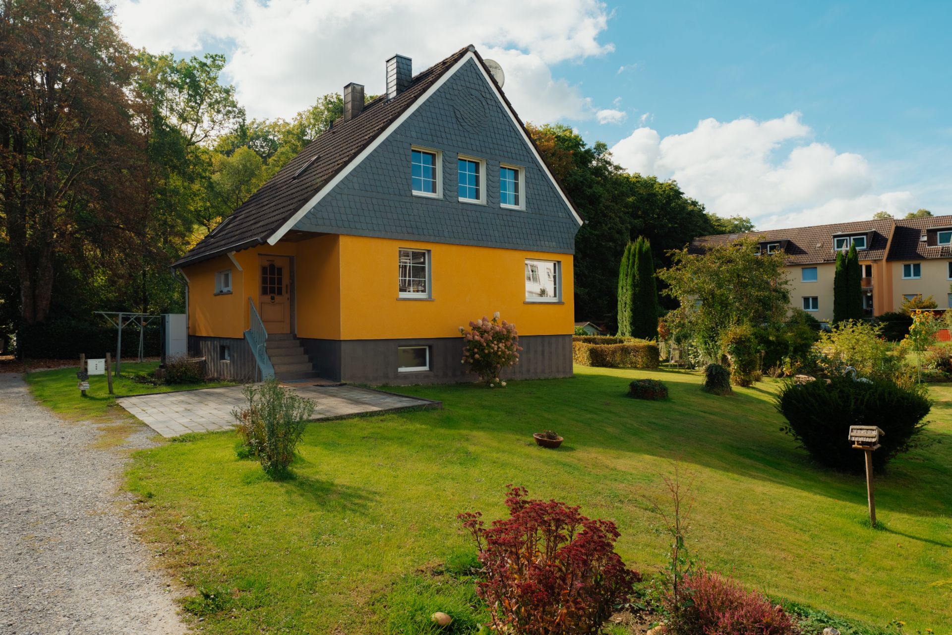 Gelbes Einfamilienhaus mit steilem Dach, Treppe und Garten auf grüner Wiese.
