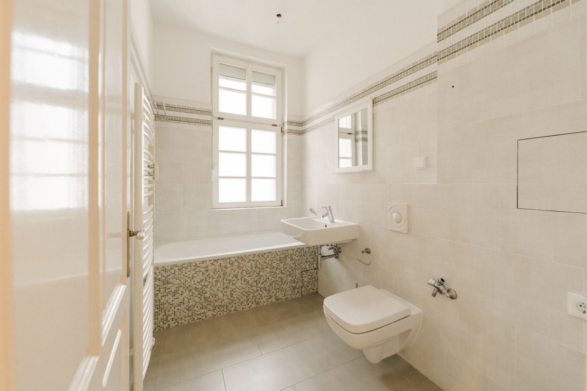 Helles Badezimmer mit Badewanne, Waschbecken, Wandspiegel und Fenster.