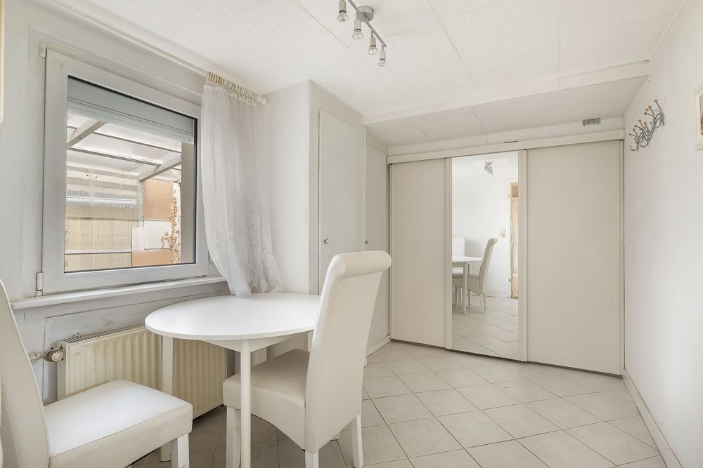 Heller Raum mit zwei weißen Stühlen, rundem Tisch, Fenster und großem Spiegel-Schrank.