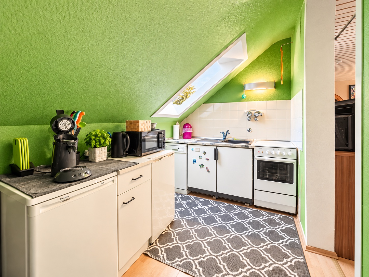 Kleine Küche mit grün gestrichenen Wänden, Dachfenster, Herd, Spüle und Küchengeräten.