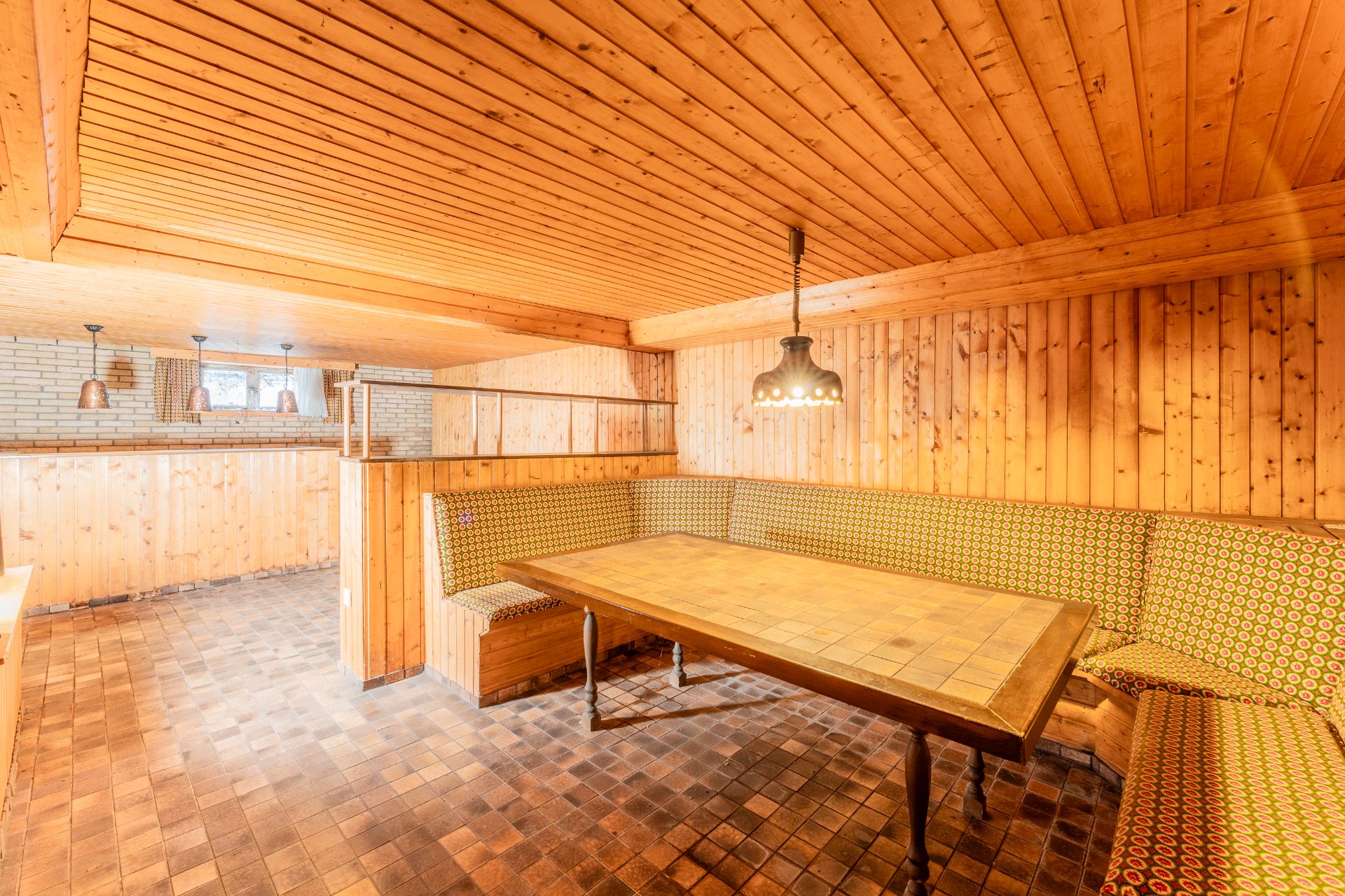 Gemütliche Sitzecke mit gemusterten Polsterbänken und Holztisch in einem holzvertäfelten Raum.