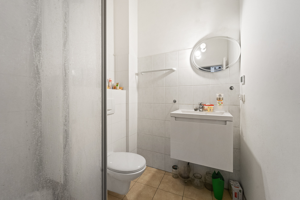 Kleines Bad mit Dusche, Toilette, Waschtisch und ovalem Spiegel an der Wand.