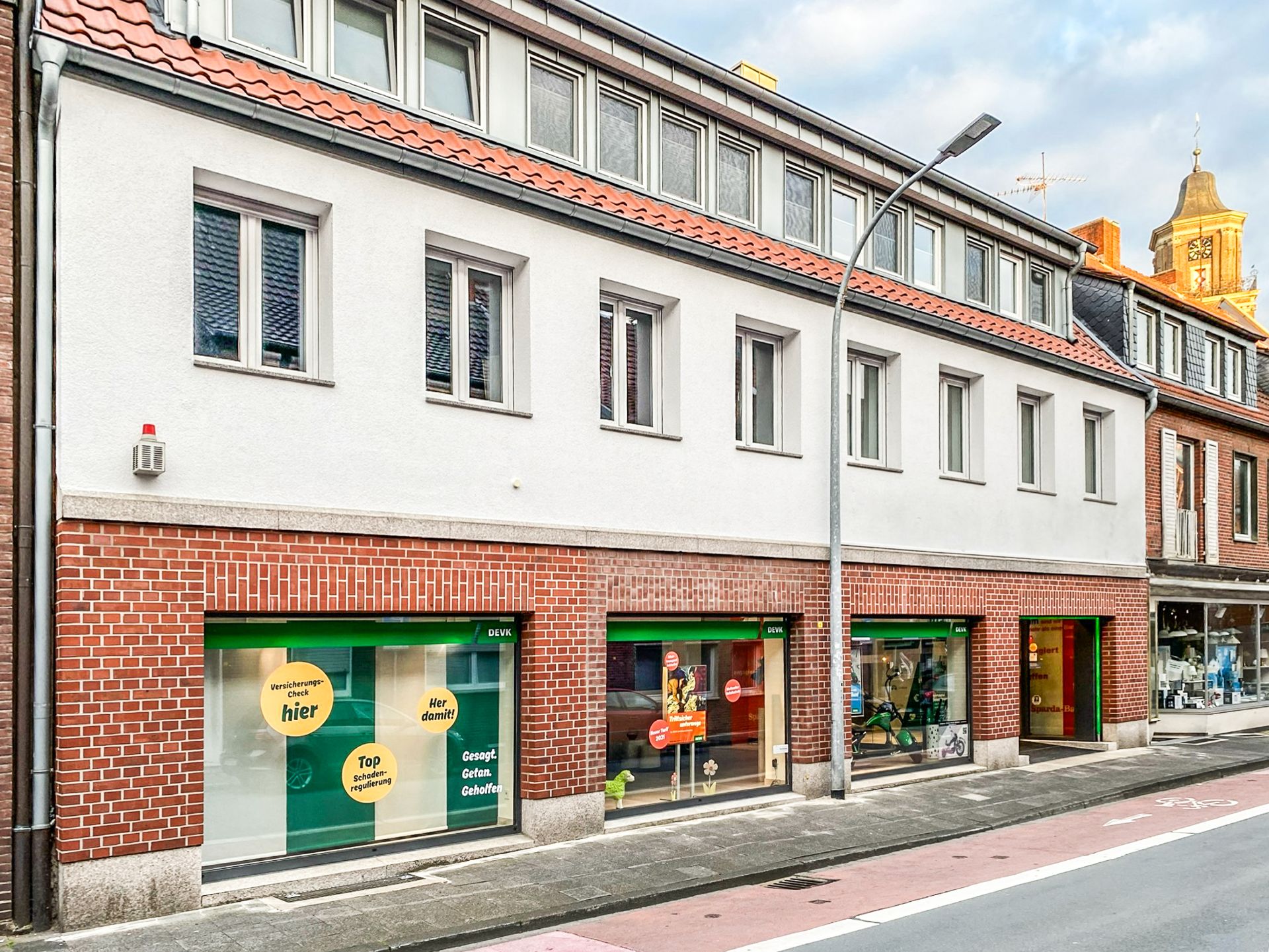 Zweistöckiges Wohnhaus mit roten Dachziegeln, mehreren Fenstern und Schaufenstern im Erdgeschoss.