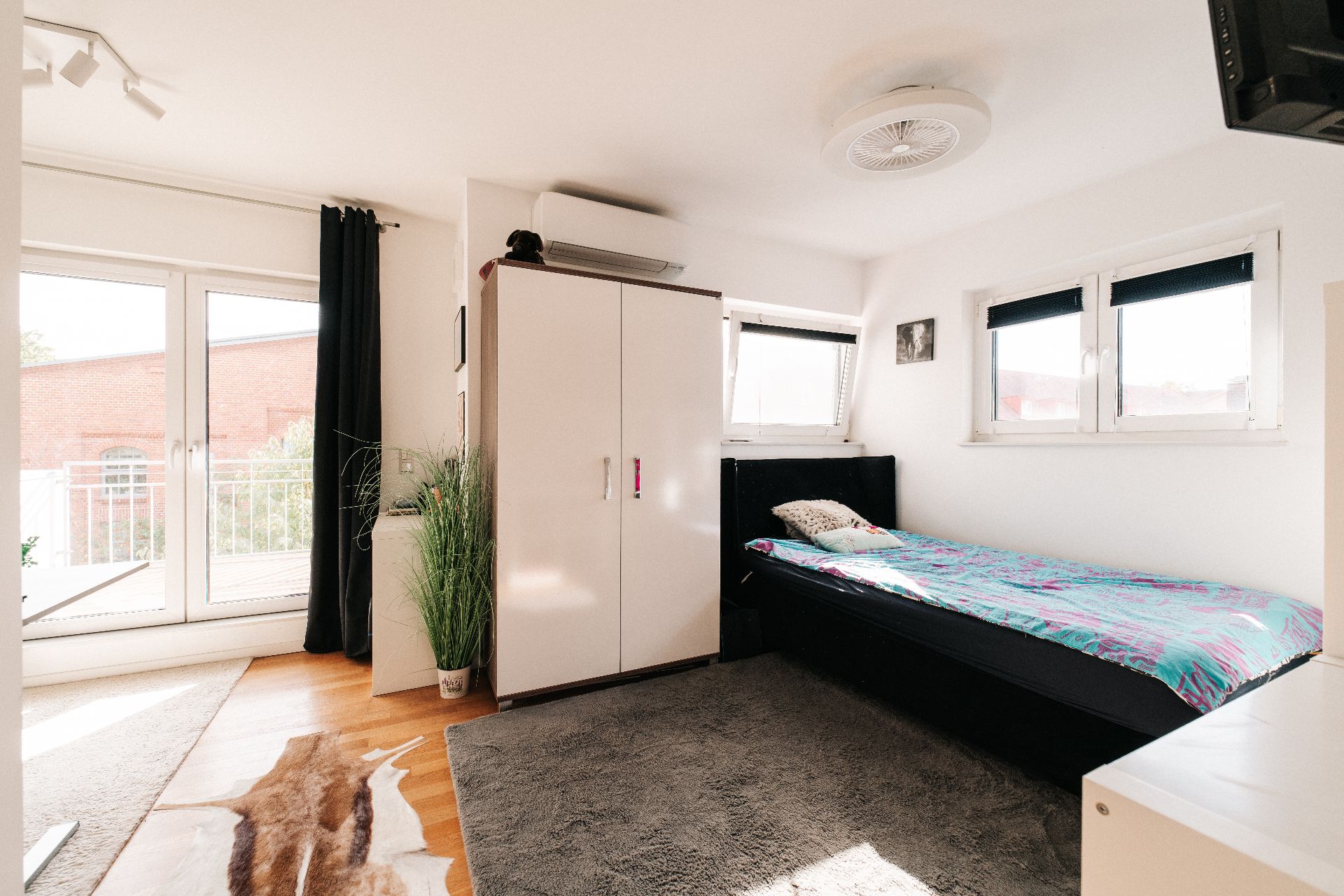 Helles Schlafzimmer mit Einzelbett, Kleiderschrank, Teppich und Zugang zu einem Balkon.