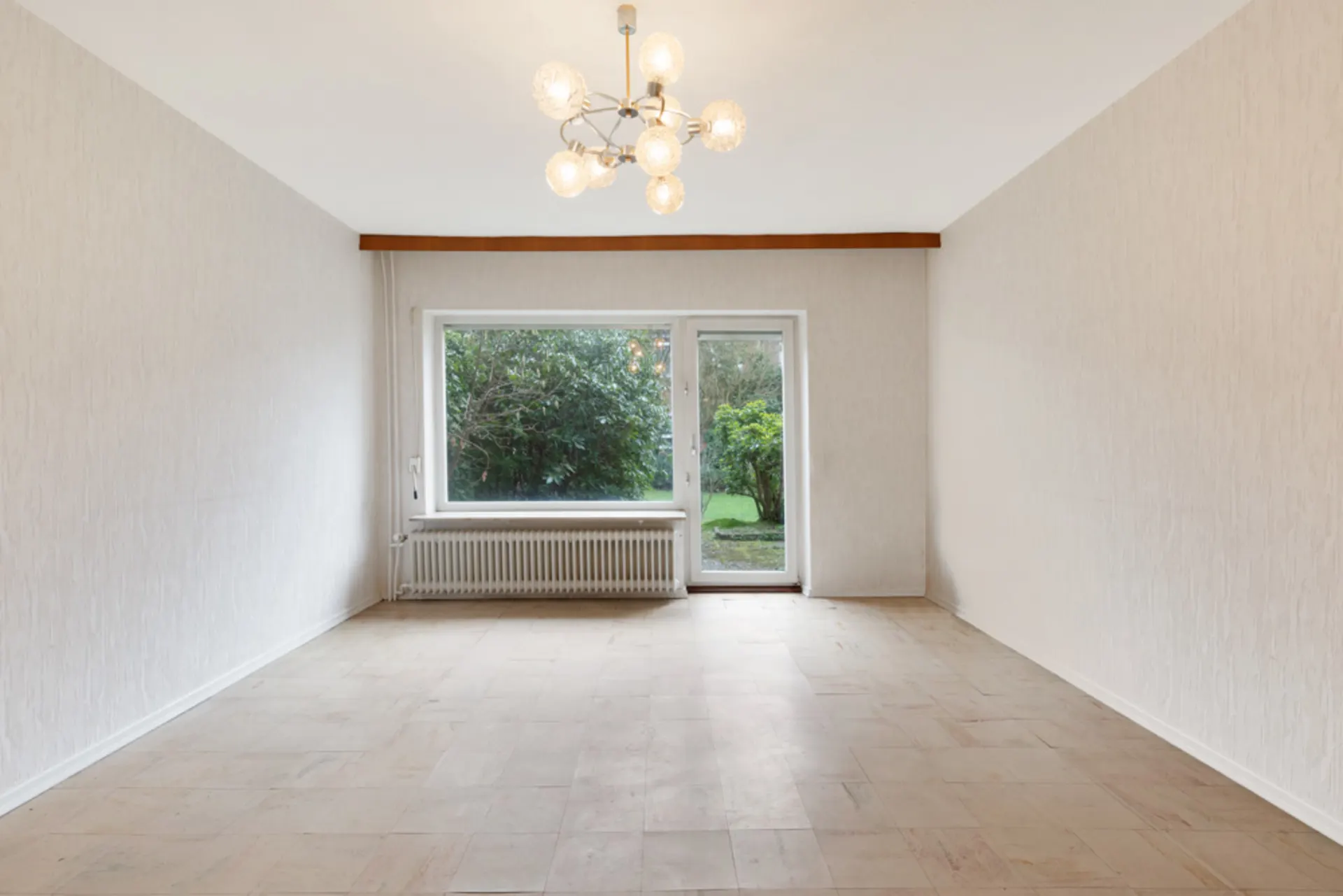 Leerer Raum mit großem Fenster und Tür zum Garten, Deckenlampe in der Mitte.