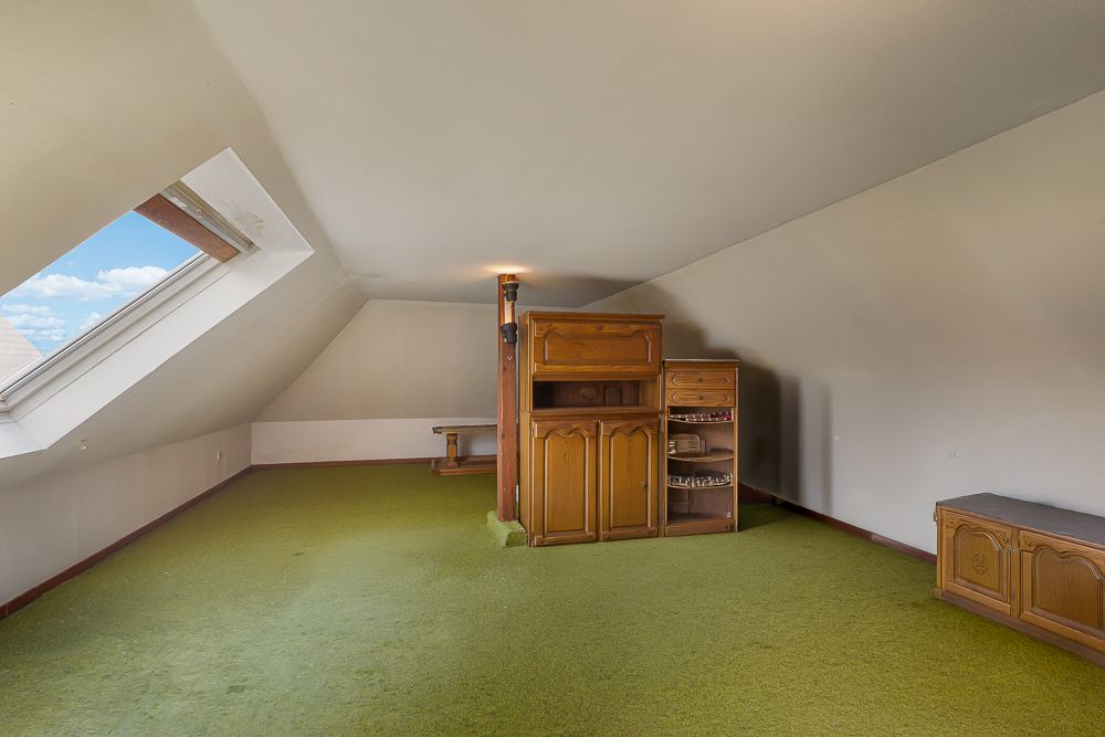 Dachzimmer mit grünem Teppich, Dachfenster und Holzschrank.