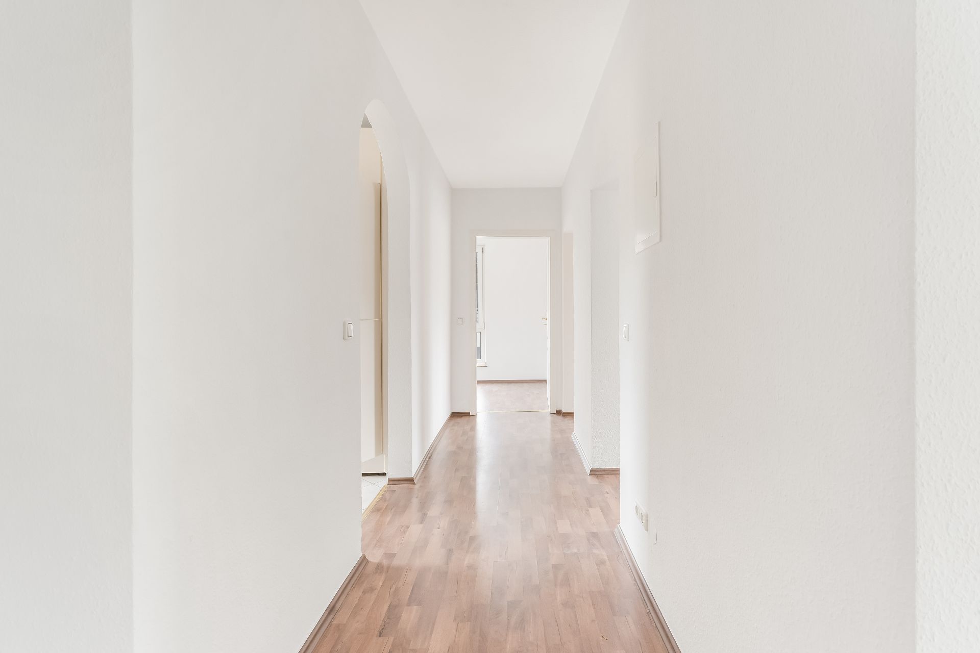 Heller Flur mit weiß gestrichenen Wänden und Holzboden, mehrere Türen führen zu weiteren Räumen.