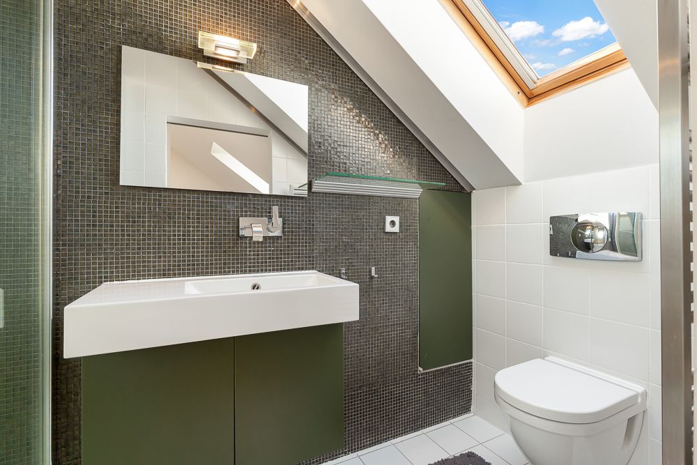 Modernes Badezimmer mit Dachfenster, Waschbecken, Spiegel und Toilette.