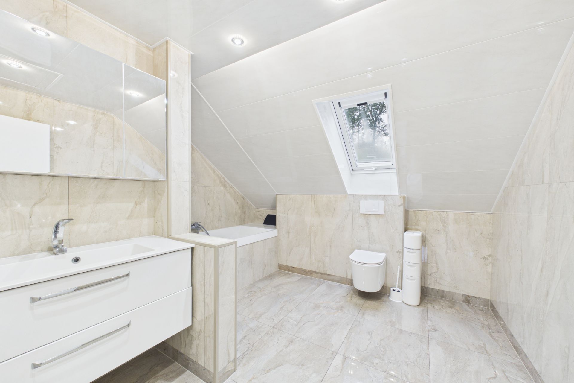 Modernes Badezimmer mit Dachschräge, Badewanne, Waschbecken, WC und Fenster.