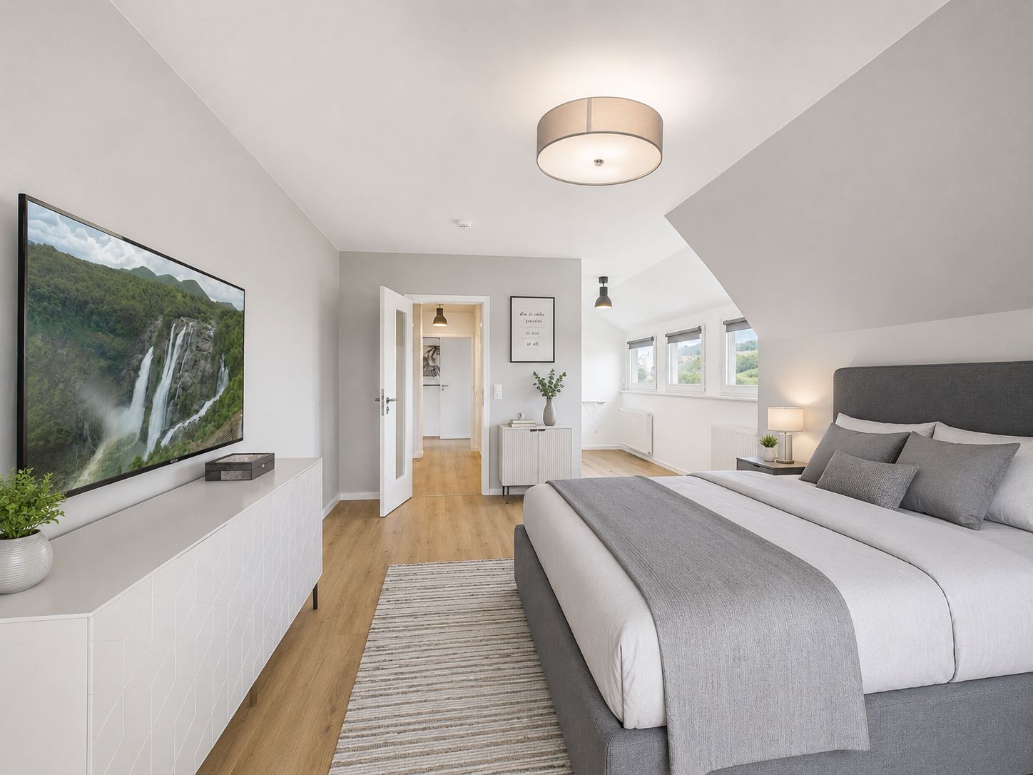 Modernes Schlafzimmer mit großem Bett, Fernseher, Kommode und mehreren Fenstern.