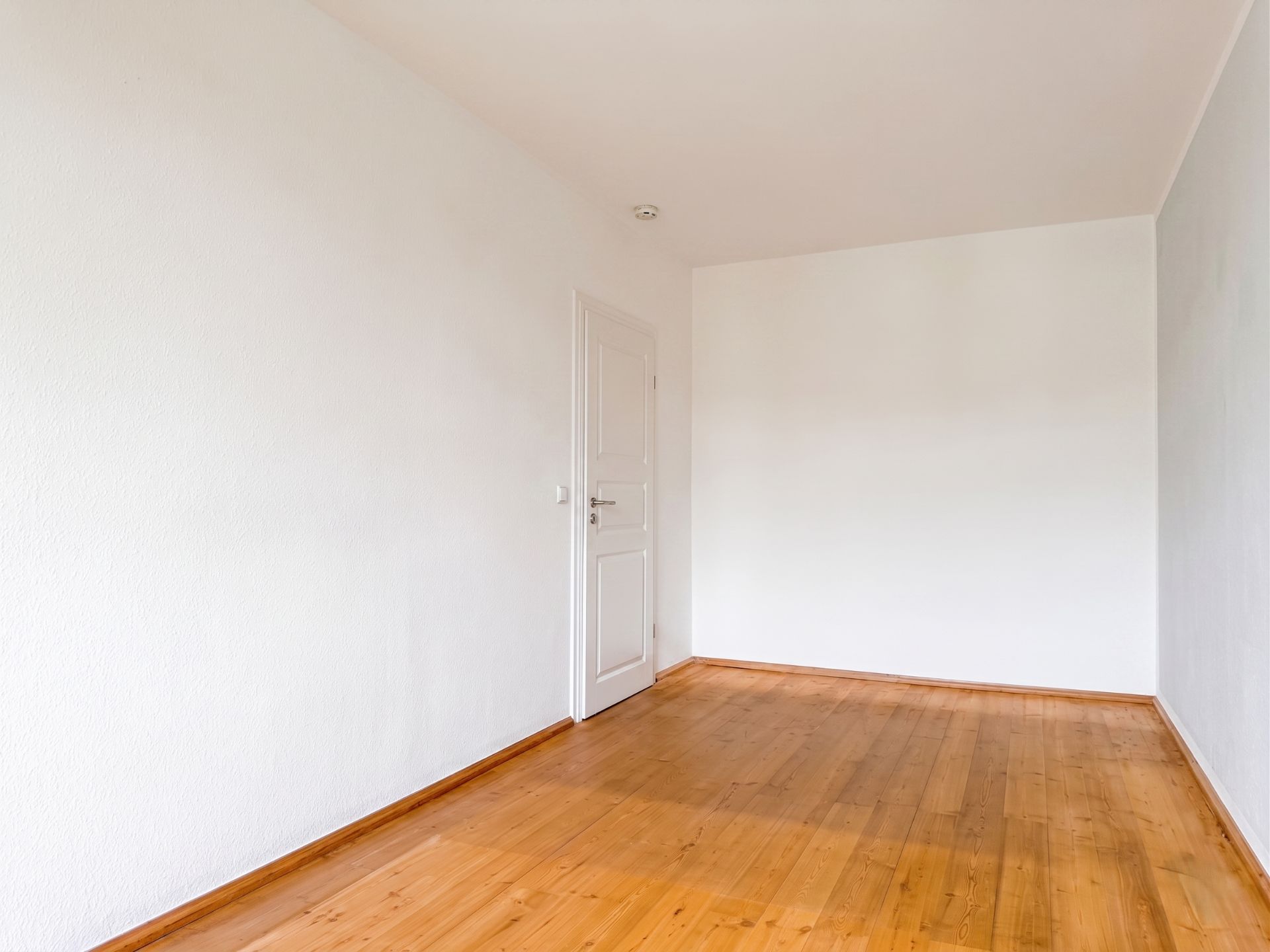 Leerer Raum mit weißer Wand, Holzboden und einer weißen Tür.