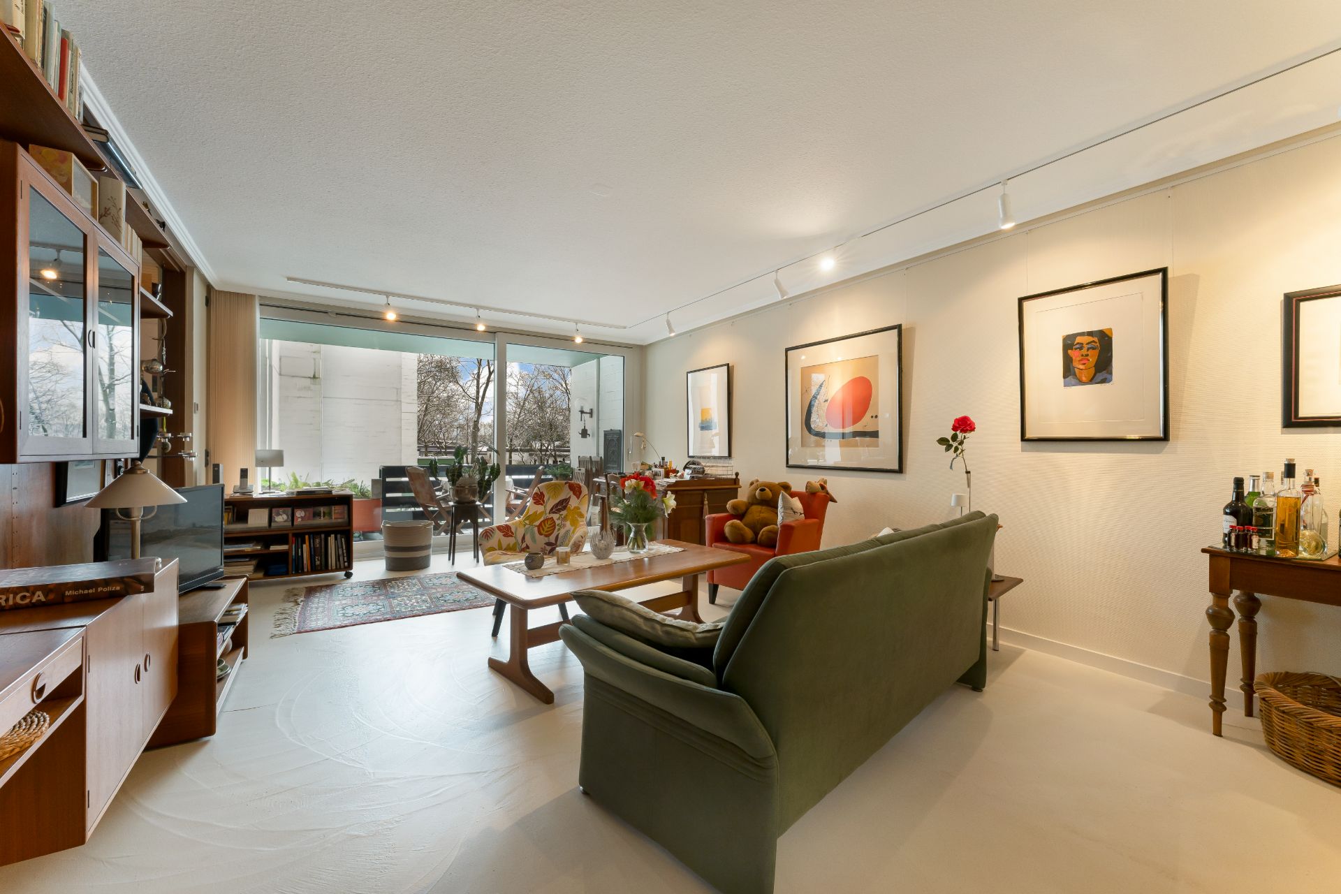 Helles Wohnzimmer mit Sofa, Couchtisch, Bilder an der Wand und Zugang zu einem Balkon.