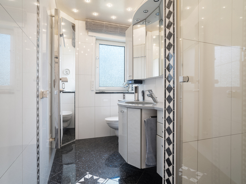 Modernes Badezimmer mit schwarzem Fliesenboden, Waschbecken, Spiegel, Fenster und Toilette.