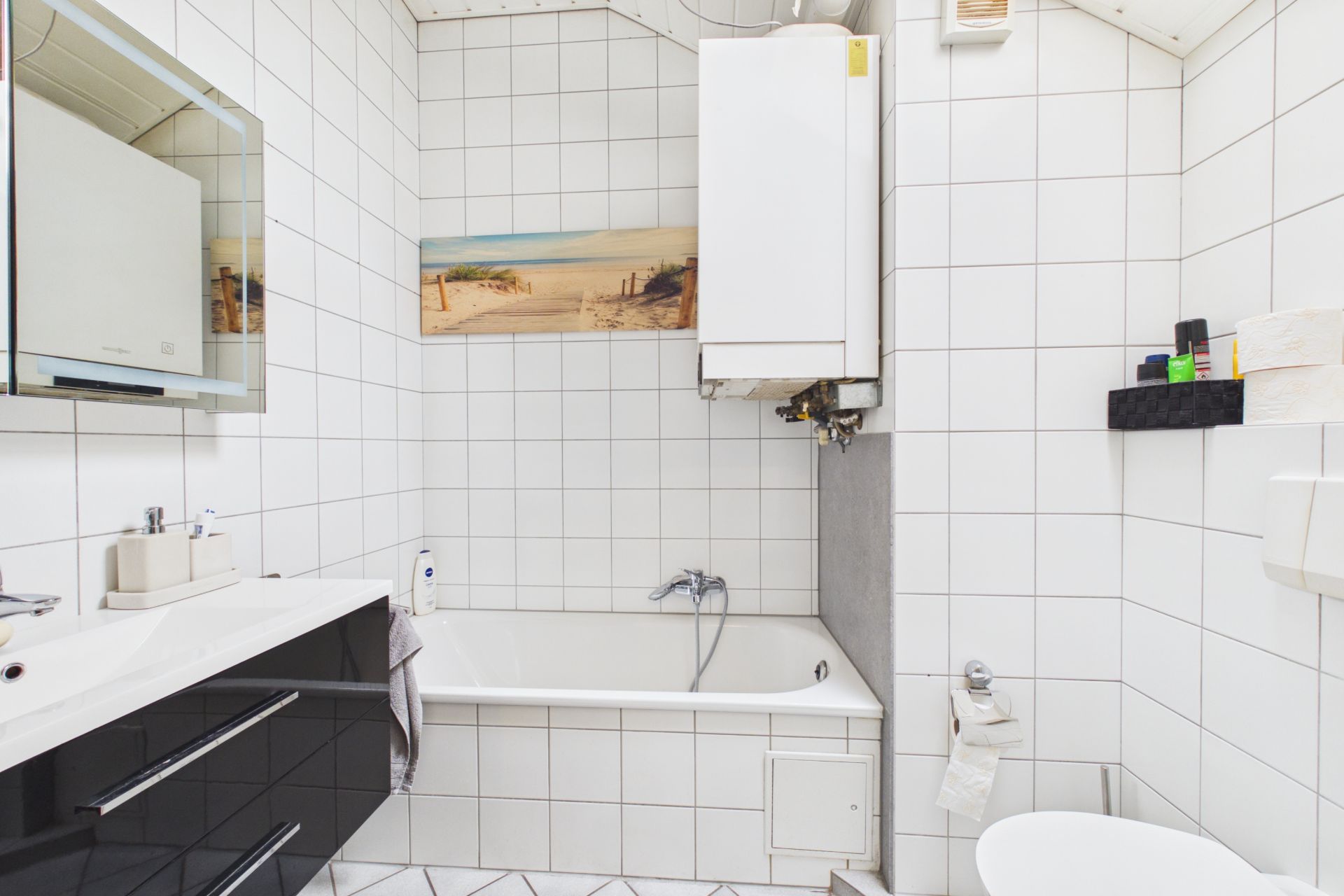 Helles Badezimmer mit Badewanne, Spiegel, Waschbecken und weißen Fliesen an den Wänden.