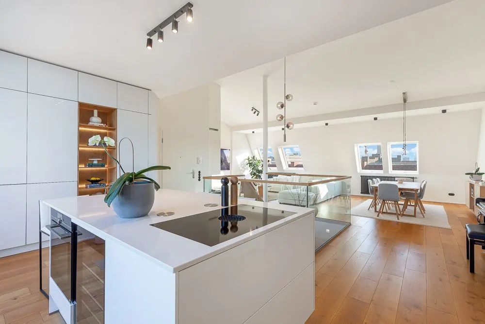 Moderne, helle Küche mit Kochinsel und Essbereich in offenem Wohnraum mit Holzfußboden.