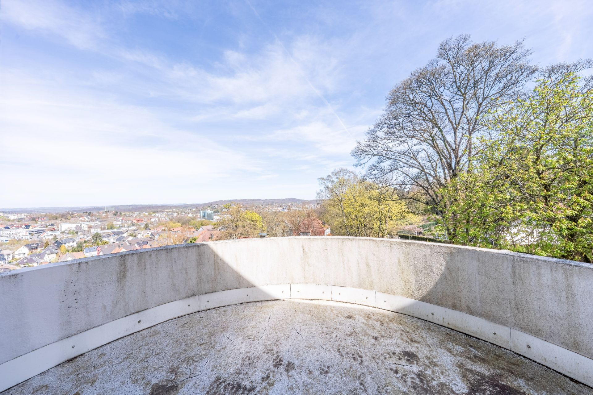 Runder Balkon mit Blick auf Bäume und Stadt bei Tageslicht.