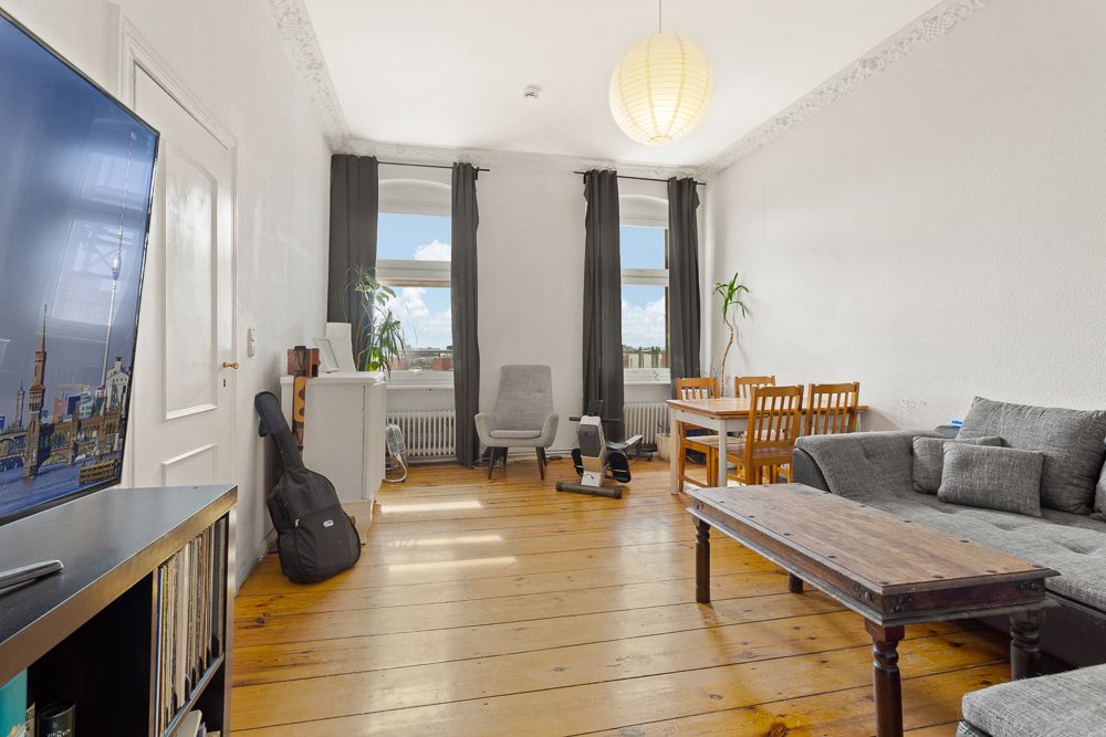 Helles Wohnzimmer mit Holzboden, grauem Sofa, Esstisch, TV und Pflanzen.