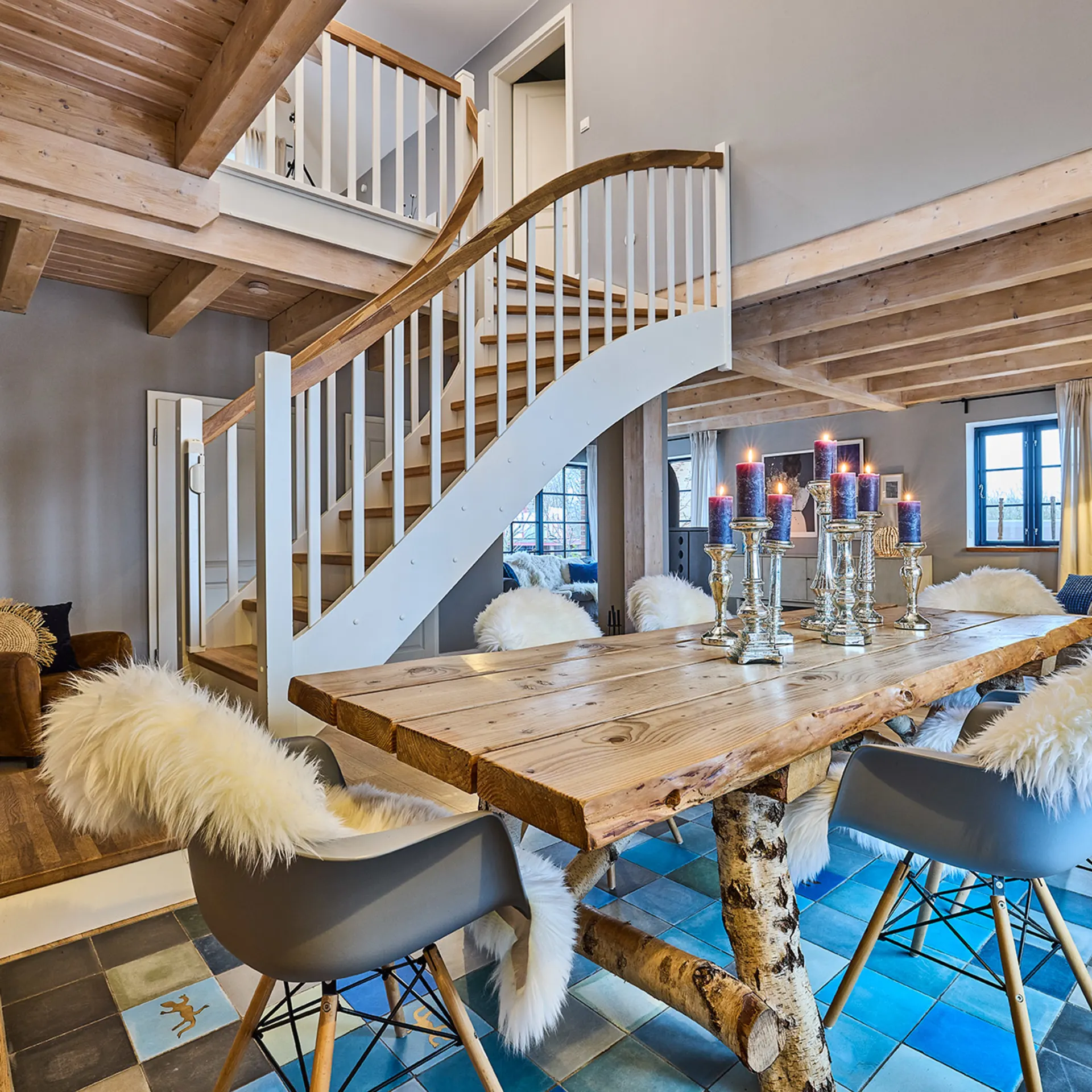Gemütliches Esszimmer mit Holztisch, Kerzenleuchtern, Fellstühlen und offener Holztreppe.
