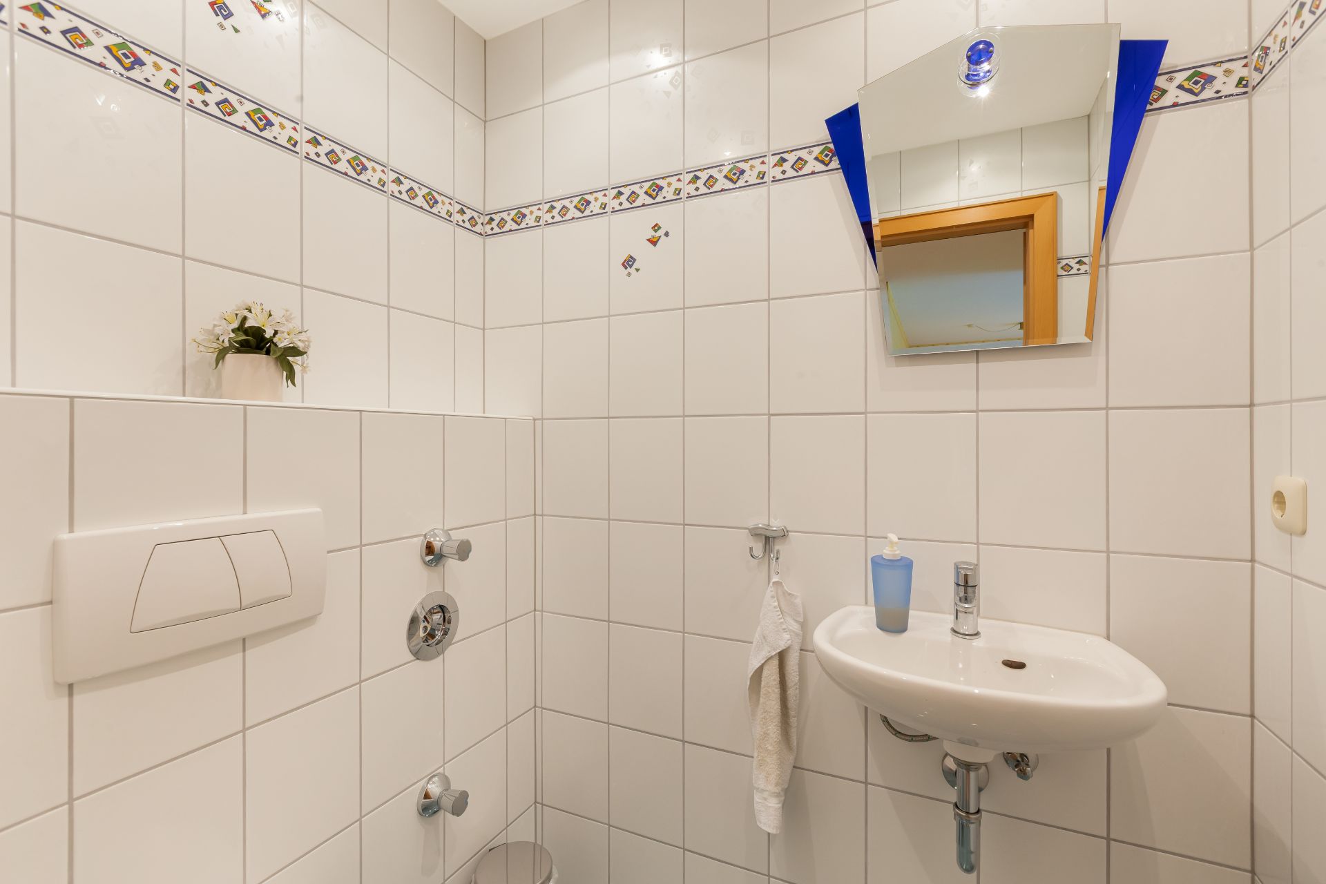 Kleines Bad mit Waschbecken, Spiegel, Handtuch und Fliesen, Blumentopf auf einer Ablage.