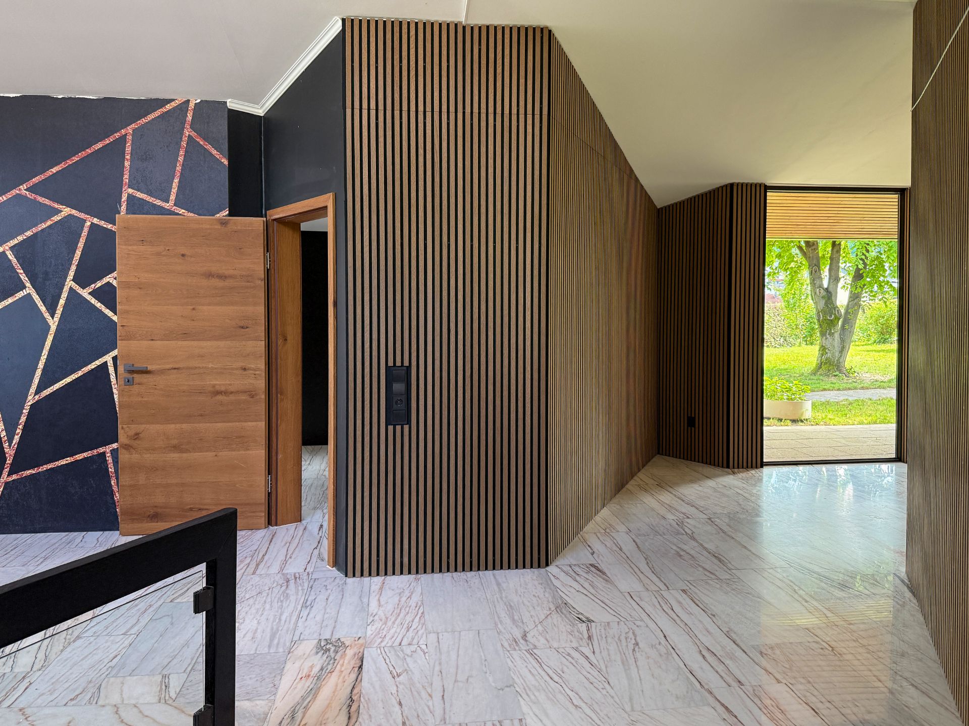 Flur mit Holzvertäfelung, Marmorboden und geometrisch gemusterter Wand, Tür zum Garten mit Blick ins Grüne.