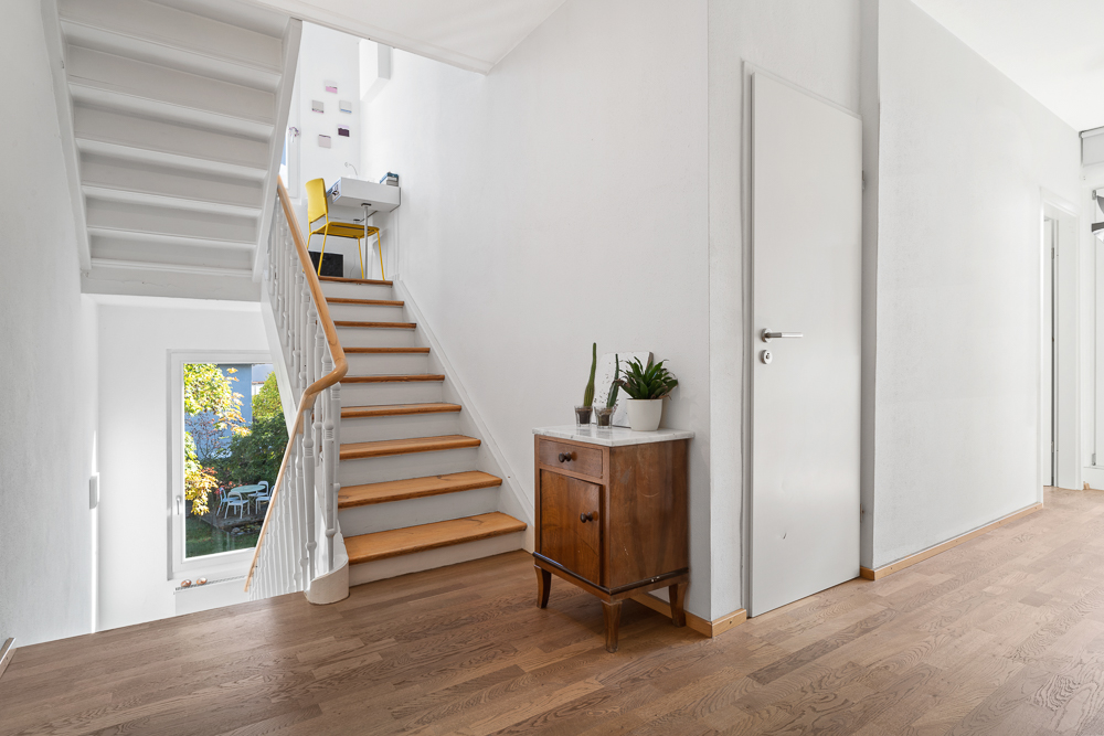 Heller Flur mit Holztreppe, Kommode mit Pflanzen und Fenster mit Blick in den Garten.
