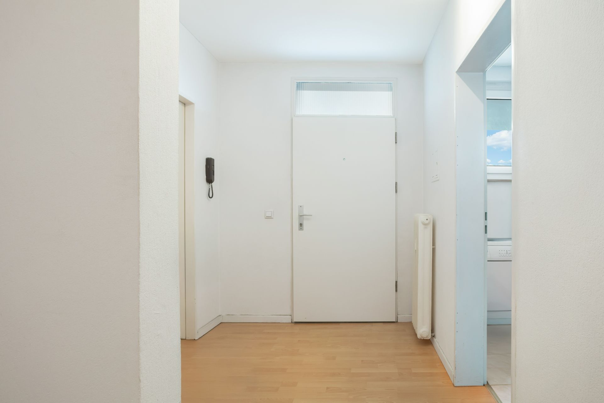 Heller Flur mit weißer Eingangstür, Holzfußboden und Blick in die Küche.