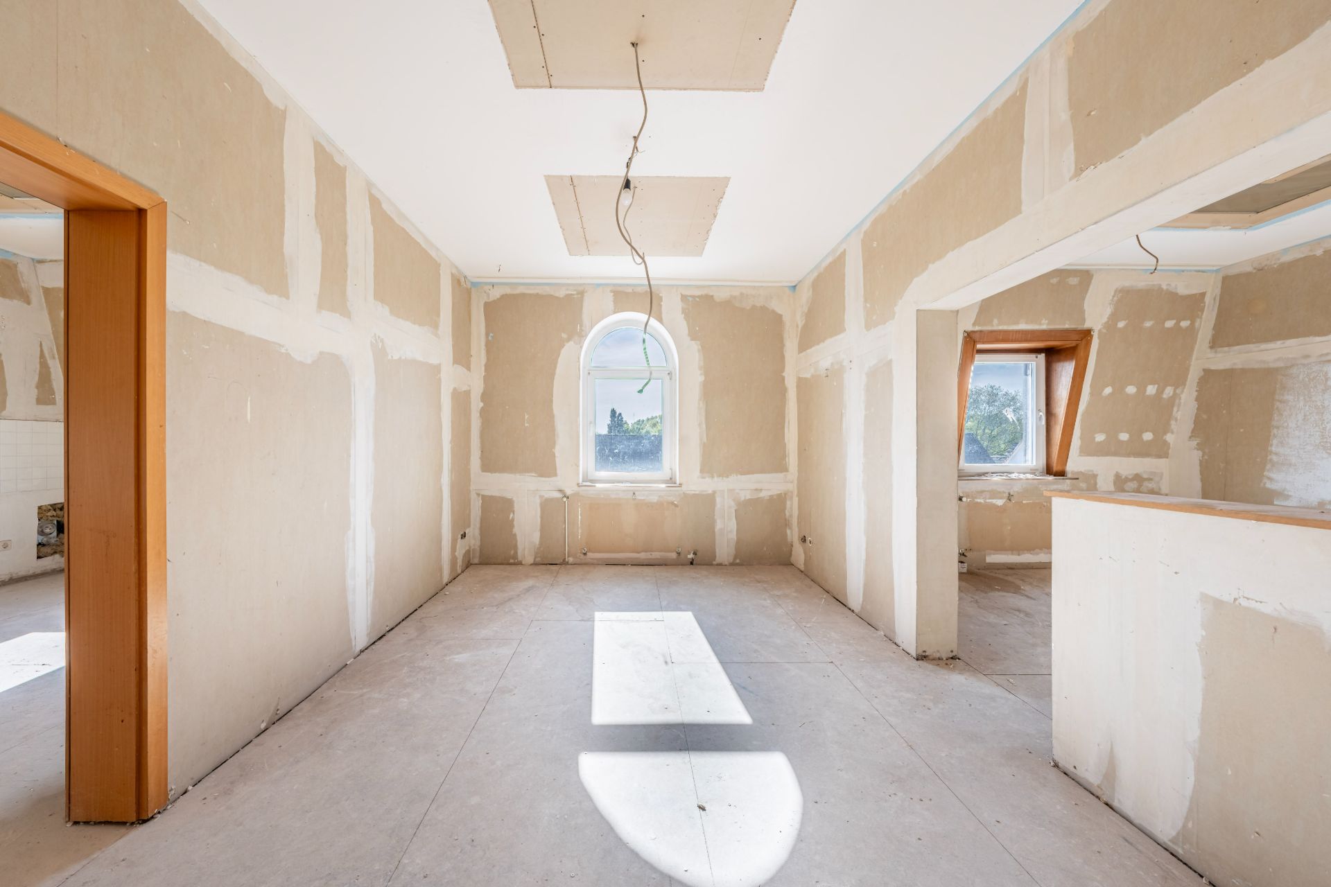 Heller Raum in Renovierung mit Putzwänden, Fenster in der Mitte, Kabel von der Decke.