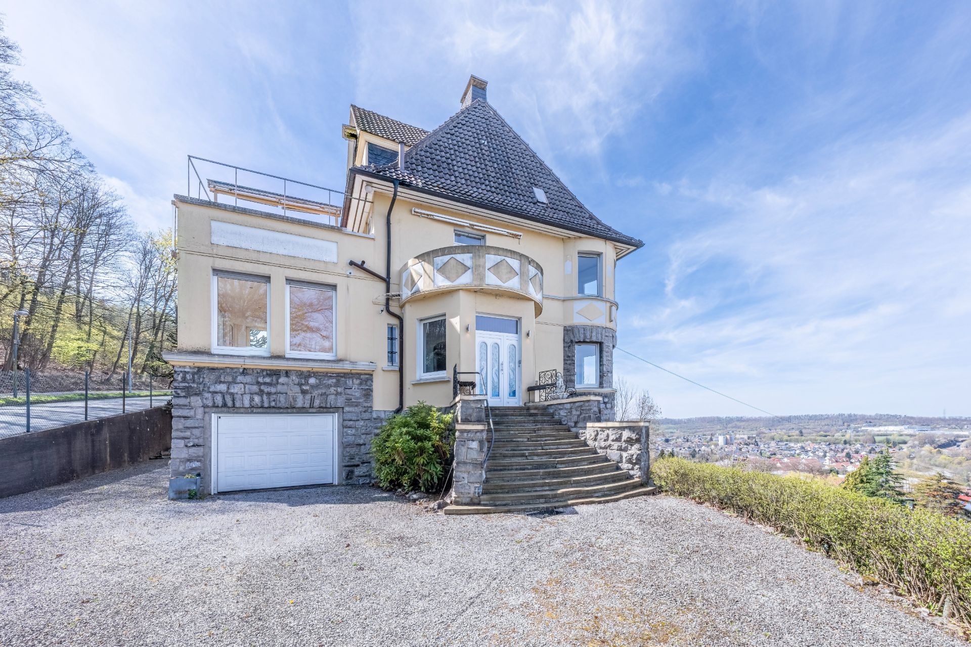 Großes Wohnhaus mit steinernen Stufen, Garage und Aussicht auf umliegende Landschaft.