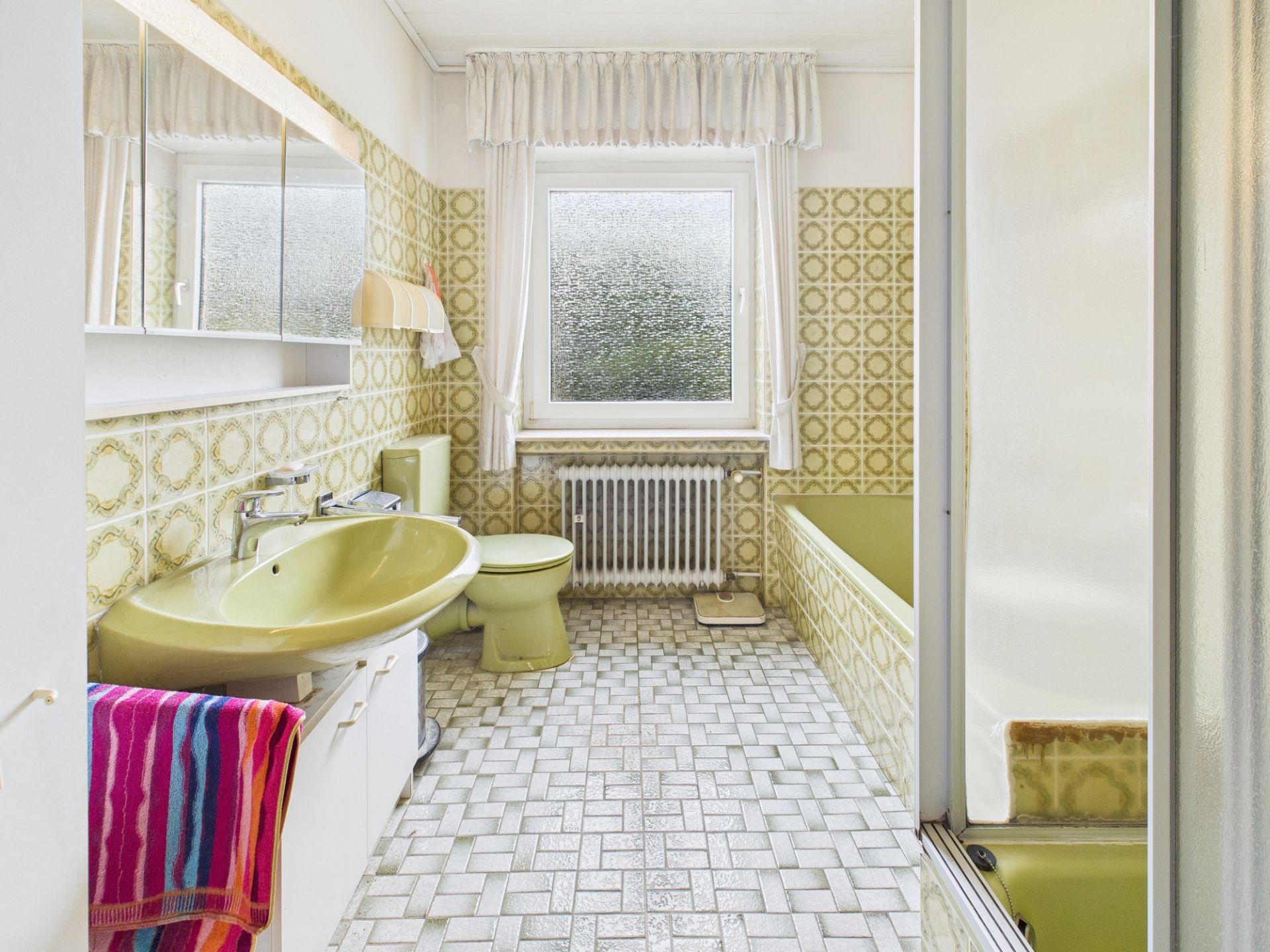 Helles Badezimmer mit grünem Waschbecken, WC, Badewanne, Spiegelschrank und Fenster.