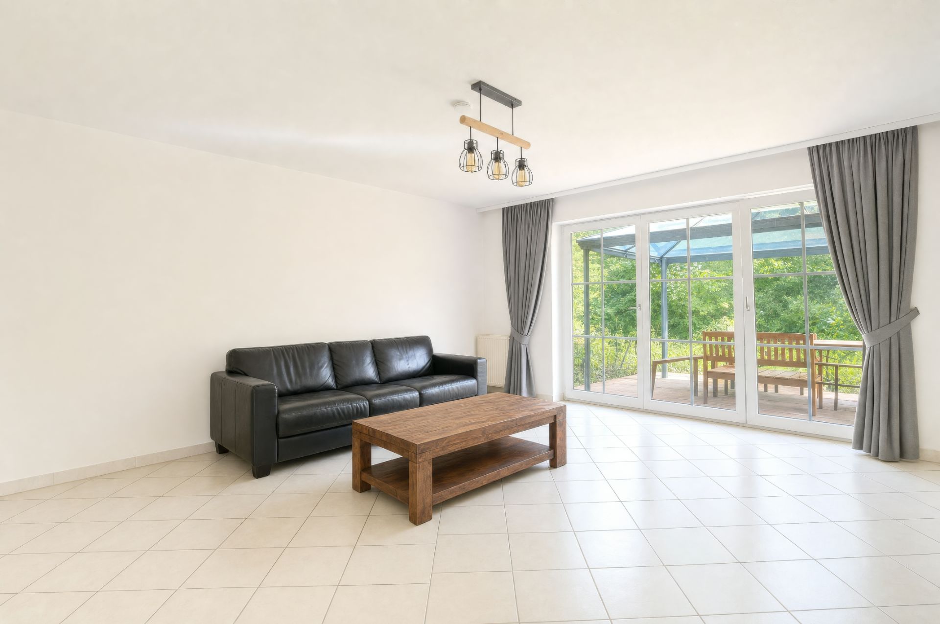 Helles Wohnzimmer mit schwarzem Sofa, Holztisch und großen Fenstern zur Terrasse.