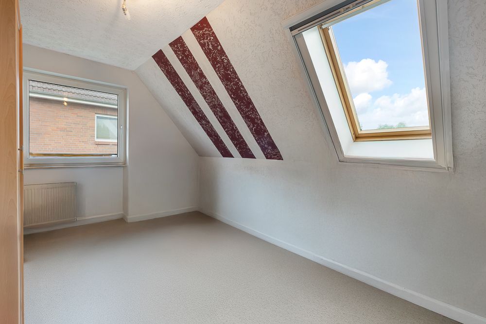 Helles Zimmer mit Dachschräge, zwei Fenstern und rot-weißen Streifen an der Wand.