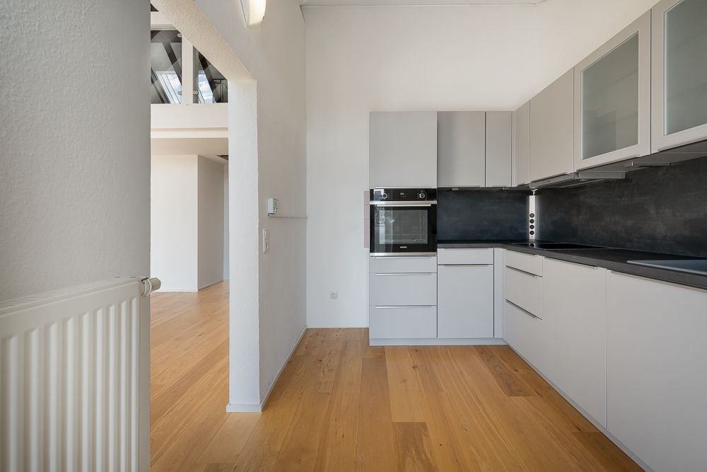 Moderne, helle Einbauküche mit Holzboden und grauen Schränken, Sicht auf angrenzenden Raum.