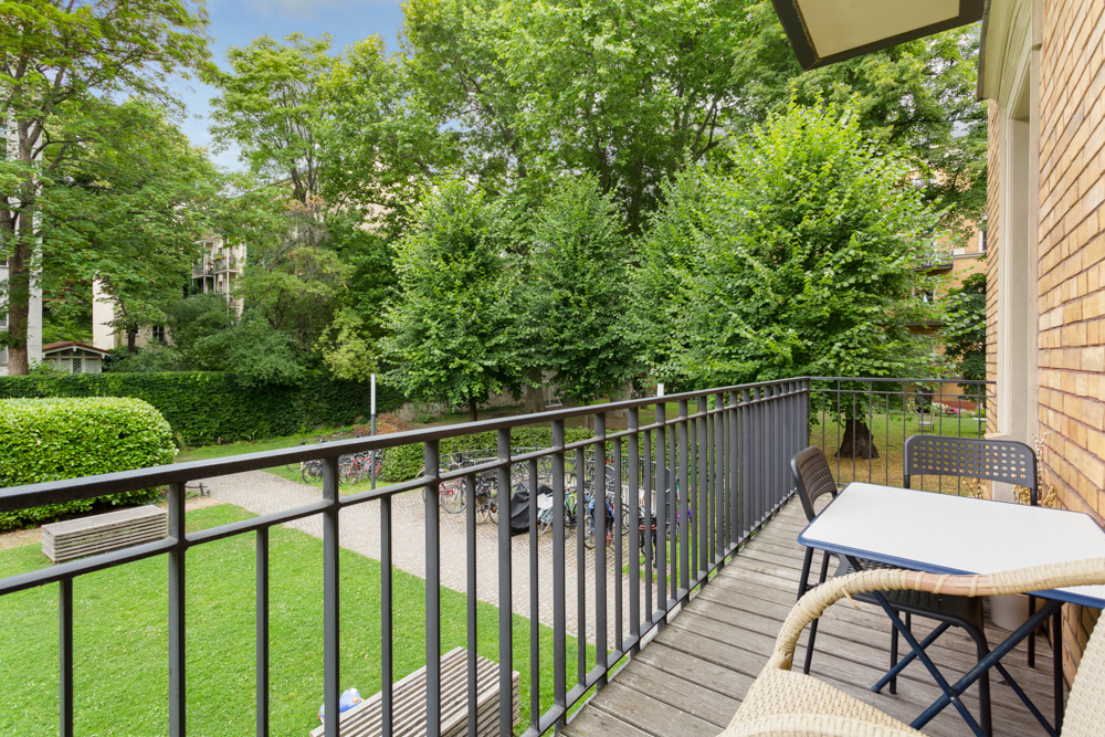 Balkon mit Tisch und Stühlen, Blick auf grünen Garten mit Bäumen und Fahrradständer.