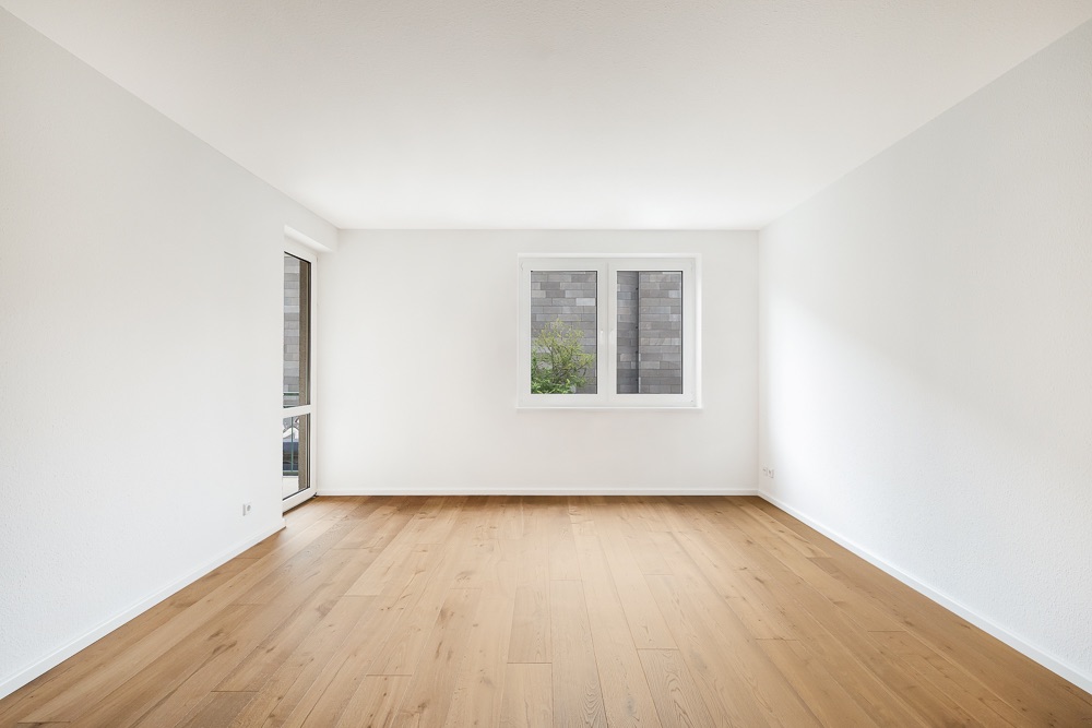 Leerer, heller Raum mit Holzfußboden, weiß gestrichenen Wänden und einem Fenster.