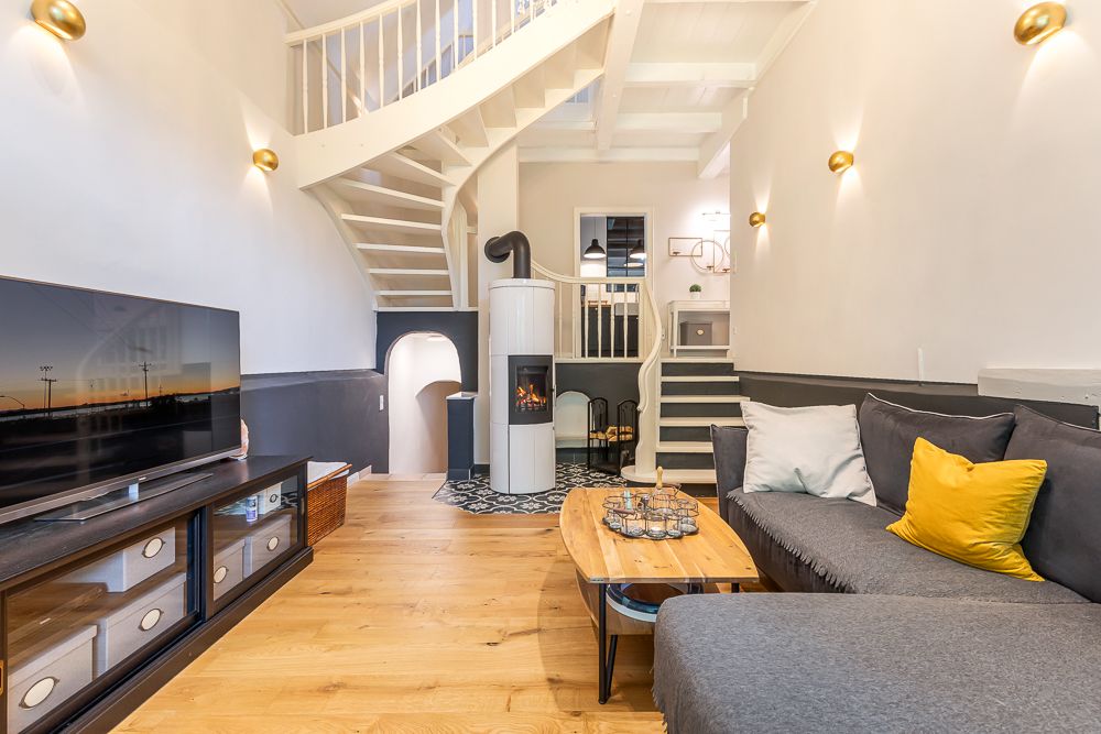 Wohnzimmer mit Ecksofa, Holzofen, Fernseher und offener Holztreppe.
