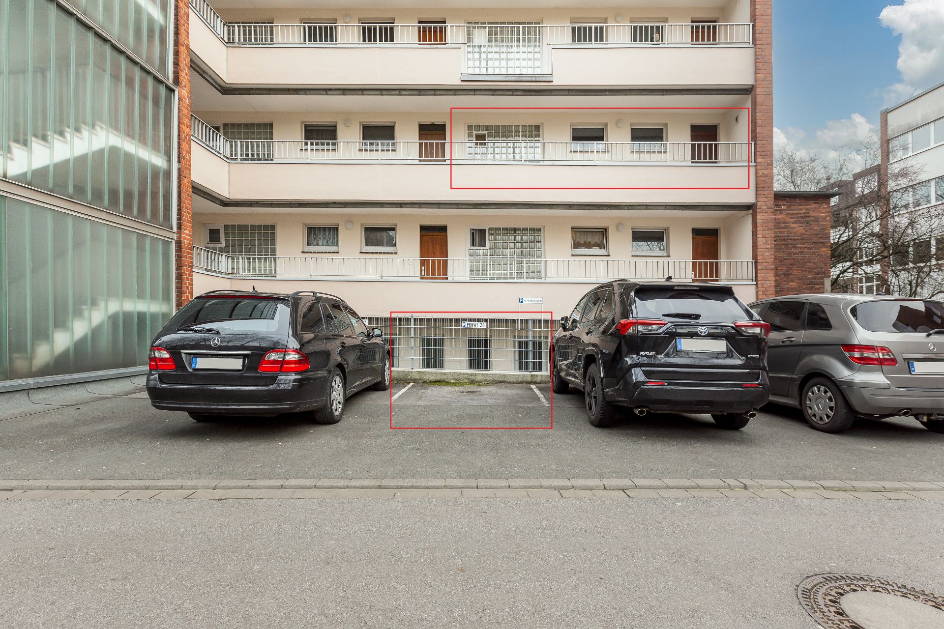 Drei parkende Autos vor einem mehrstöckigen Wohngebäude mit Balkonen und Parkplätzen.