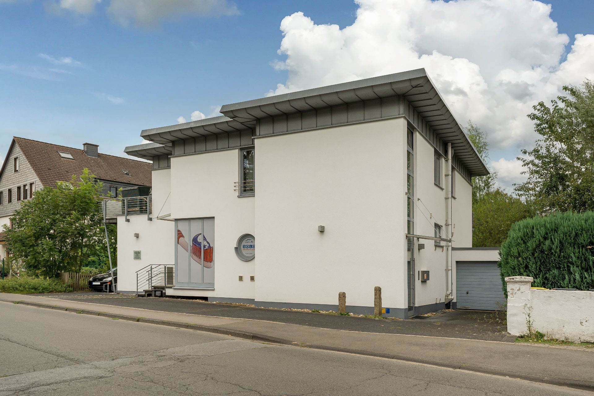 Modernes, zweistöckiges Wohnhaus mit Flachdach, weißer Fassade und Garage, an einer Straße gelegen.