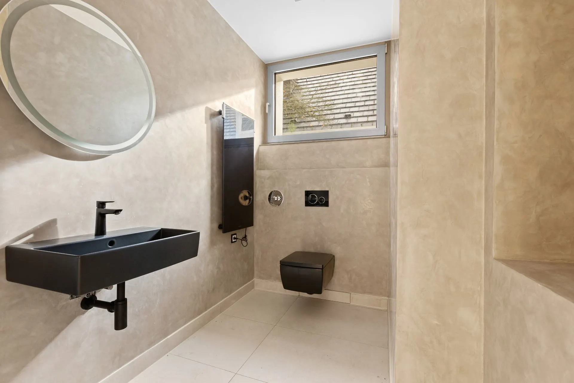Modernes Bad mit schwarzem Waschbecken, rundem Spiegel und hängender Toilette.