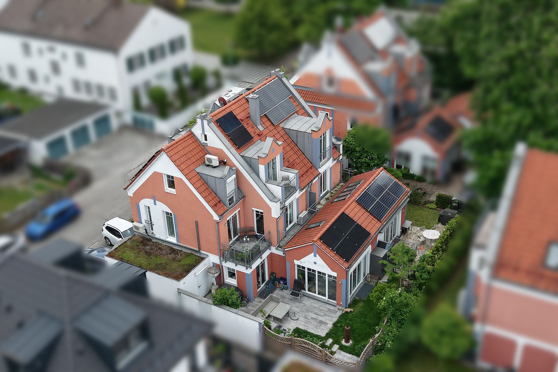 Luftaufnahme eines modernen Wohnhauses mit roten Dächern, Solarpanels und kleinem Garten.