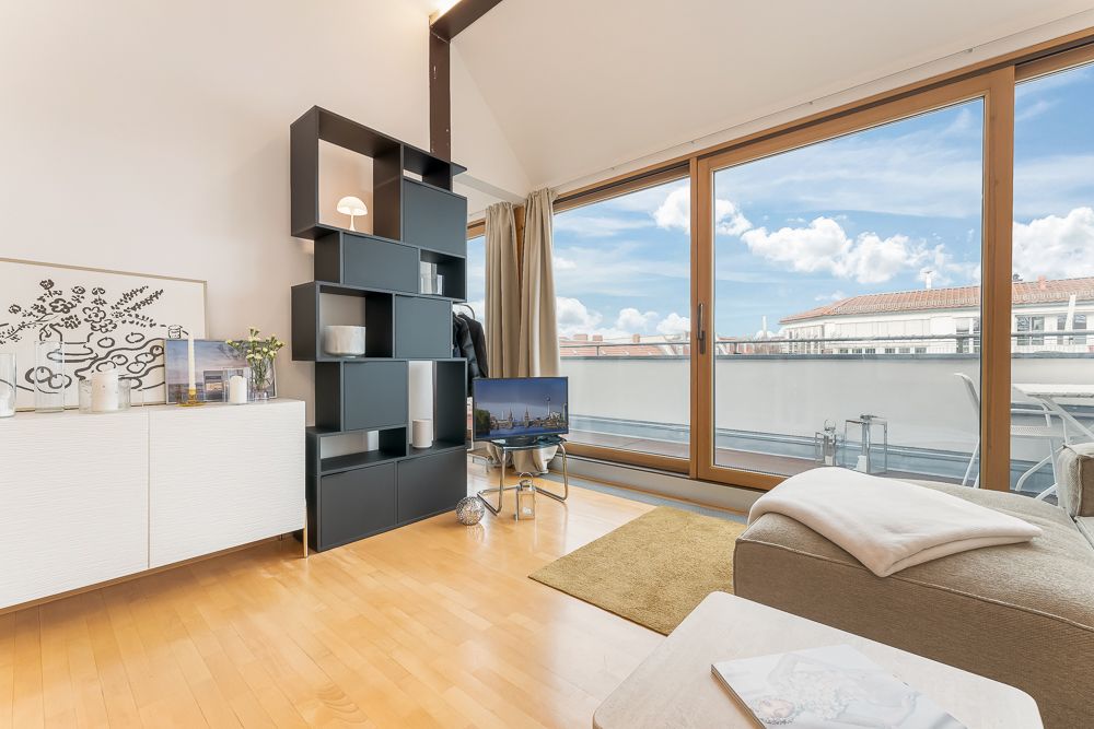 Modernes Wohnzimmer mit Holzfußboden, Regal, Sofa und großen Fenstern zu einem Balkon.