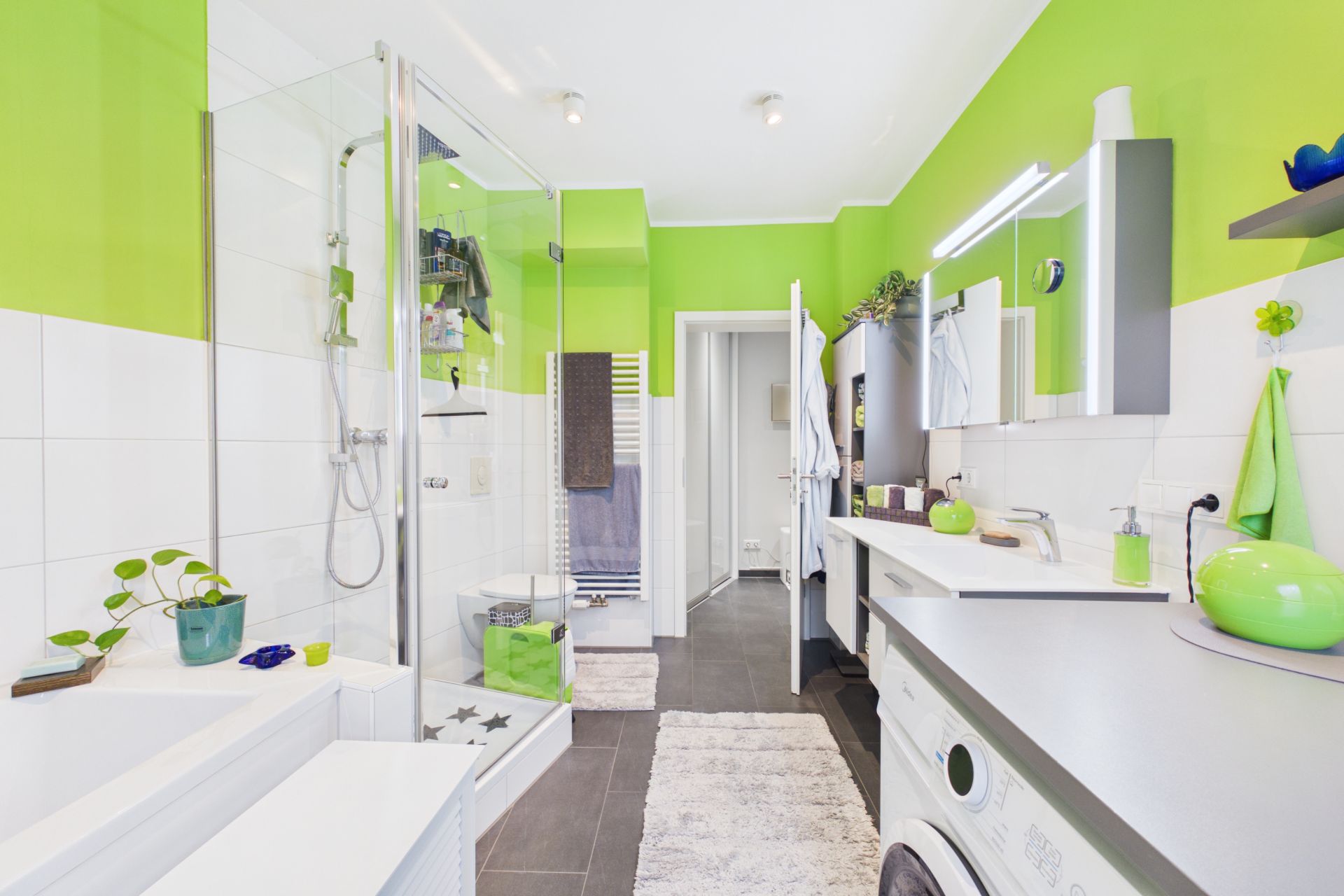 Modernes Bad mit grünen Wänden, Dusche, Badewanne, Waschmaschine und großem Spiegel.