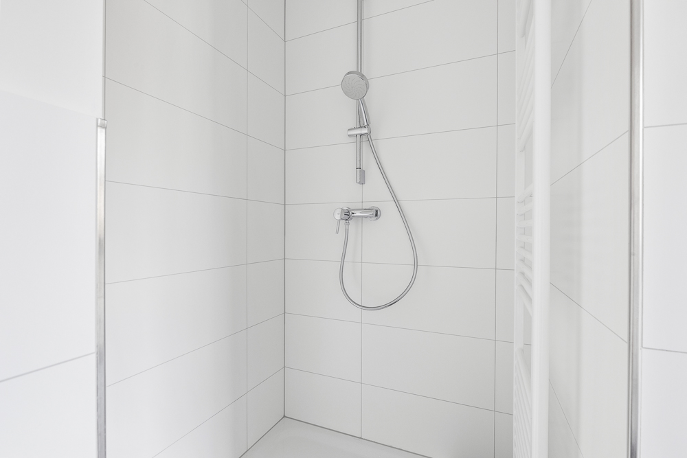 Moderne, weiße Dusche mit Handbrause und großen Fliesen.
